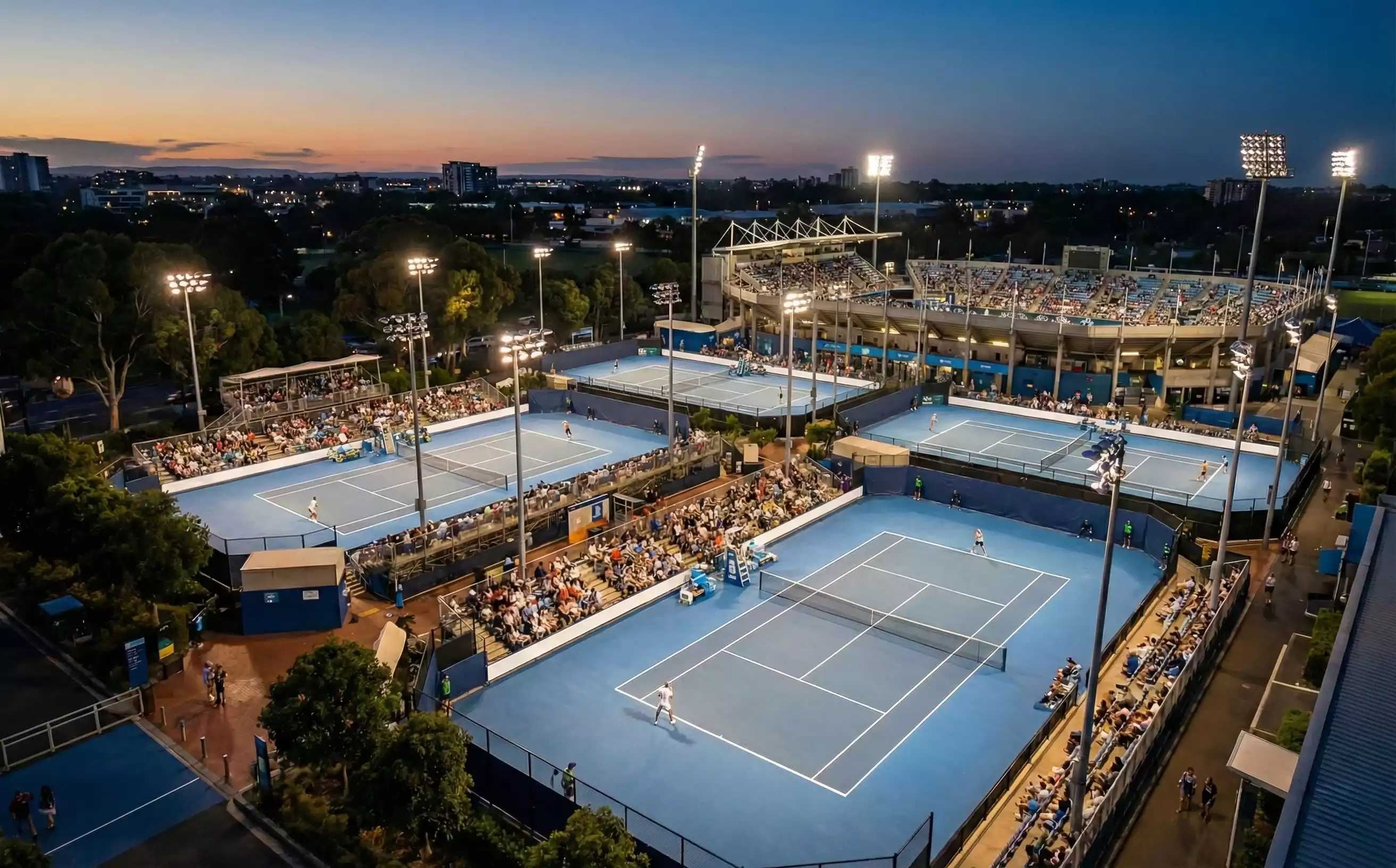 Tennisarena bei Abenddämmerung mit beleuchteten Plätzen und Zuschauern